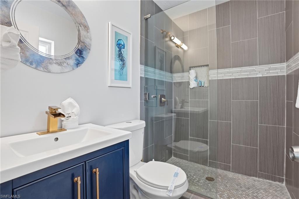 Bathroom featuring a glass-enclosed shower with vertical gray tile, a mosaic tile accent band, and a built-in niche - Virtually Edited Image