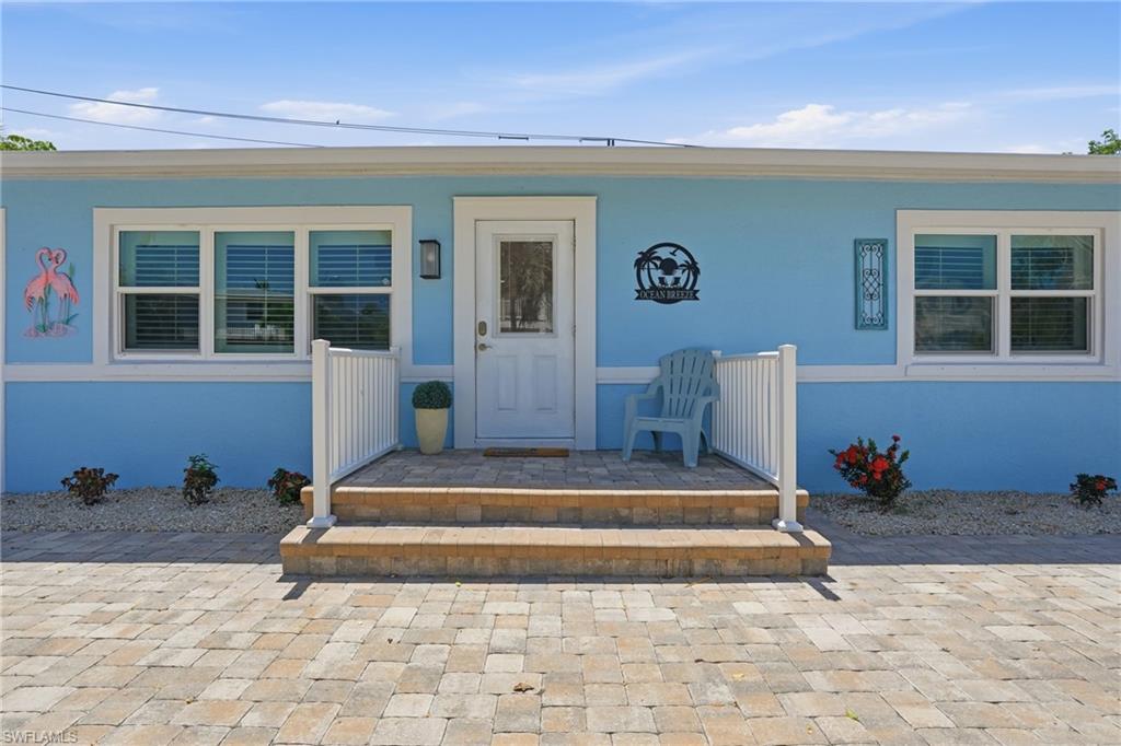 Light blue exterior with white trim, featuring a paver driveway, matching paver porch steps, white railing, and a window with blinds - Virtually Edited Image