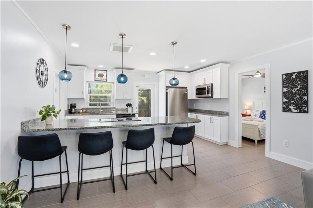 Spacious kitchen featuring an extended peninsula with seating, shaker-style cabinetry, stainless steel appliances, granite countertops, and tile flooring - Virtually Edited Image