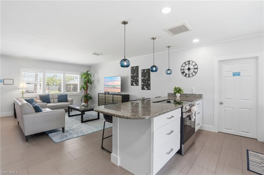 Open-concept living space featuring a kitchen island with granite countertops, stainless steel appliances, and pendant lighting - Virtually Edited Image