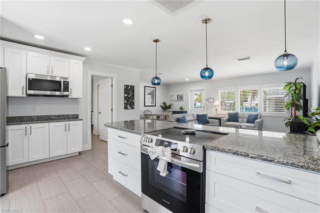 Open-concept kitchen featuring white shaker cabinetry, stainless steel appliances, and a central island with a built-in range - Virtually Edited Image
