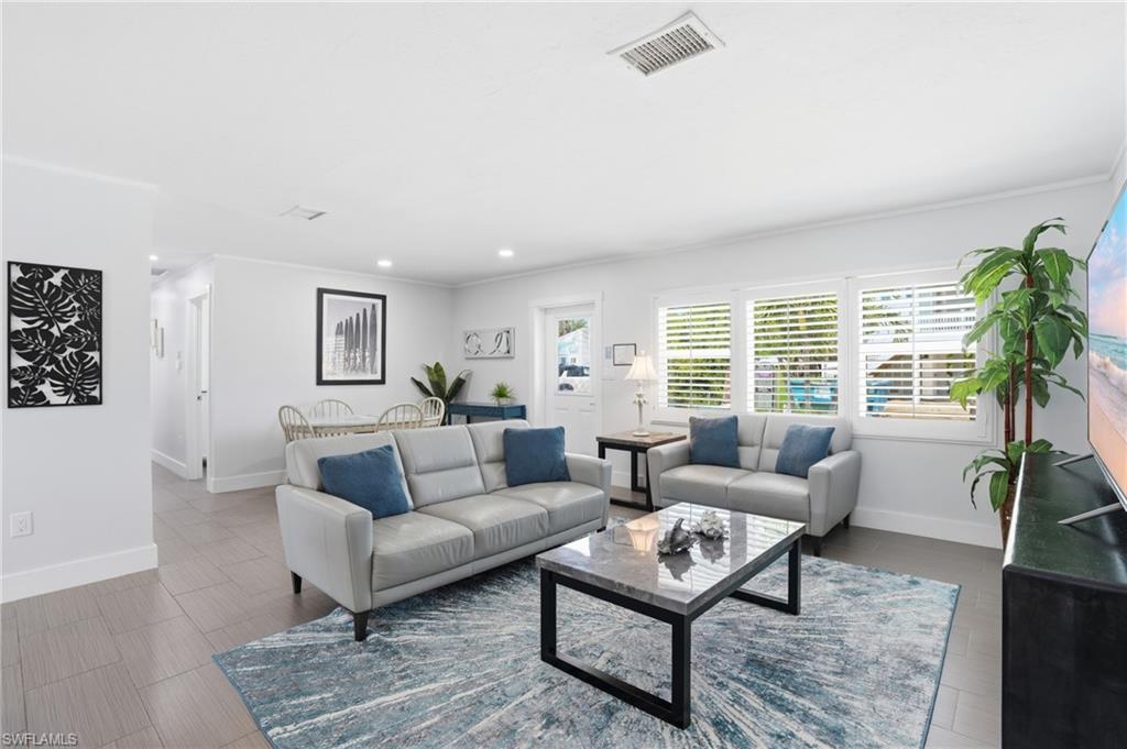 Bright living area featuring wood-finish flooring, white plantation shutters, and recessed lighting - Virtually Edited Image