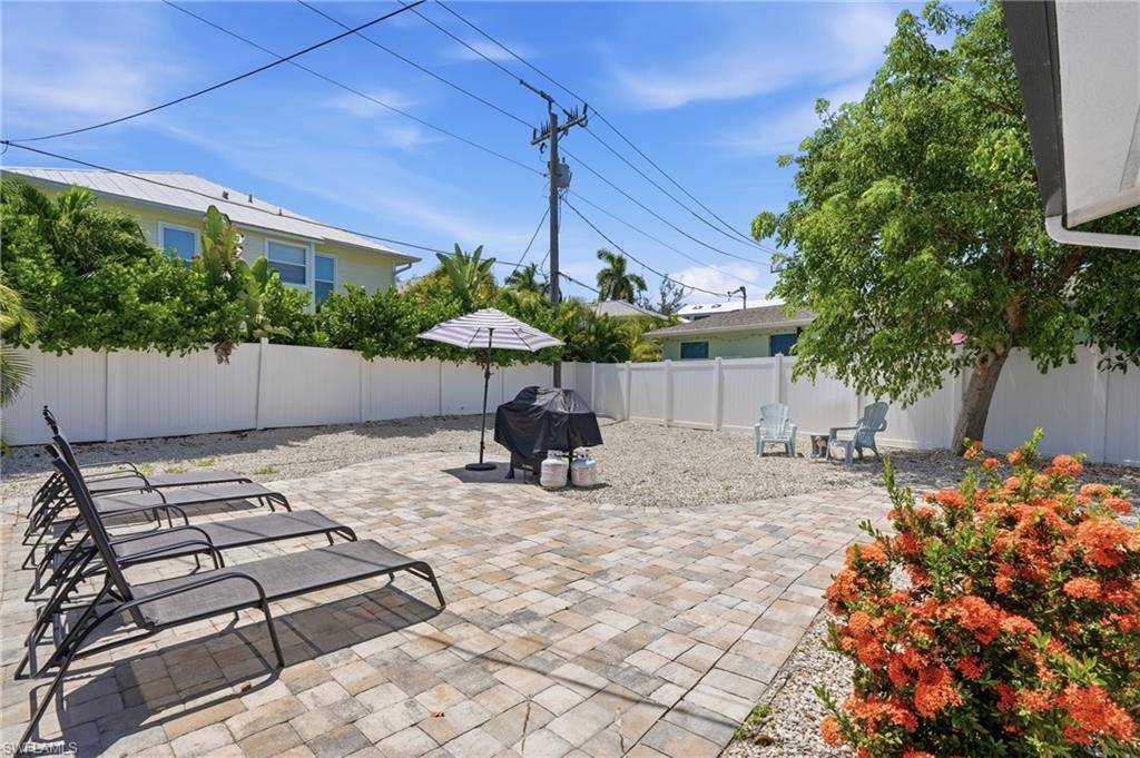 Paved patio area featuring paver stones, a white privacy fence, and mature landscaping - Virtually Edited Image