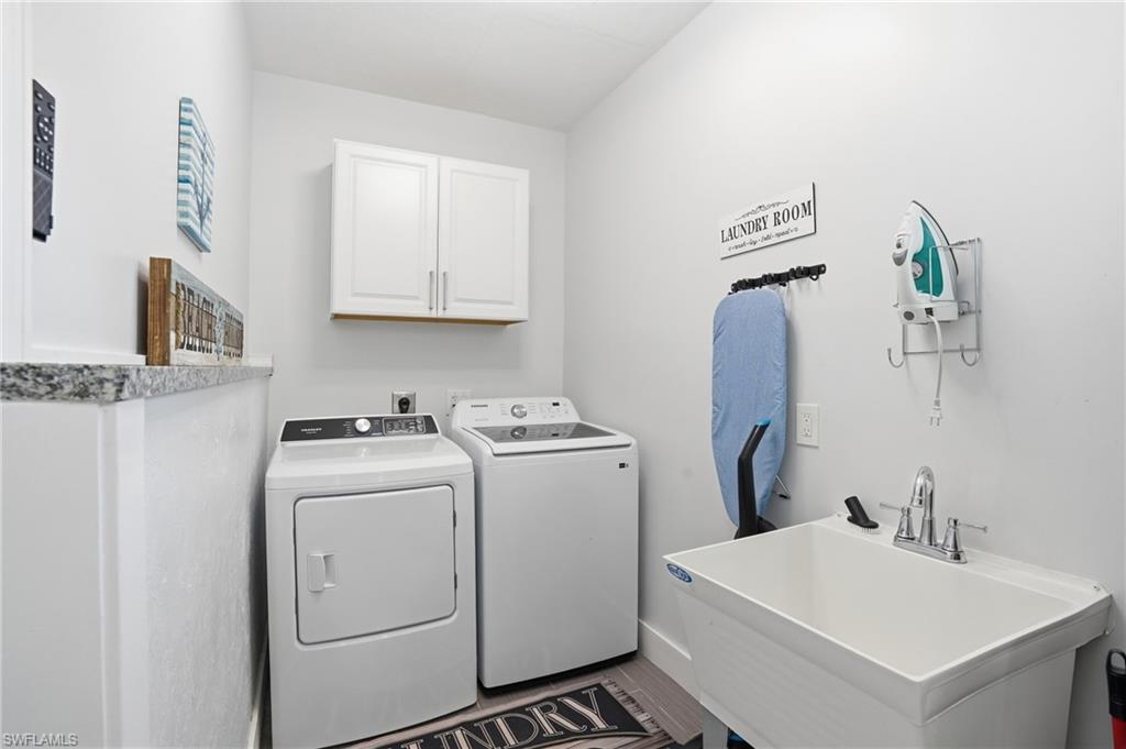 Dedicated laundry area featuring a utility sink with chrome faucet, granite countertop, built-in upper cabinetry, and wood-finish flooring - Virtually Edited Image