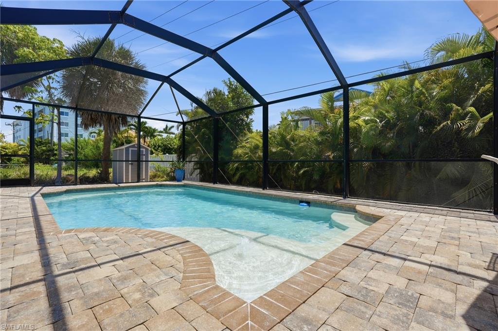 Screened-in pool area featuring a rectangular pool with an integrated sun shelf, surrounded by a paver patio - Virtually Edited Image