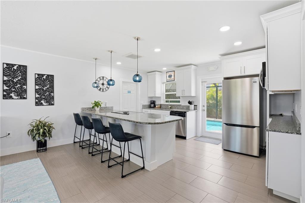 Kitchen featuring an expansive island with seating, white cabinetry, integrated stainless steel appliances, granite countertops, and direct access to an outdoor pool area - Virtually Edited Image