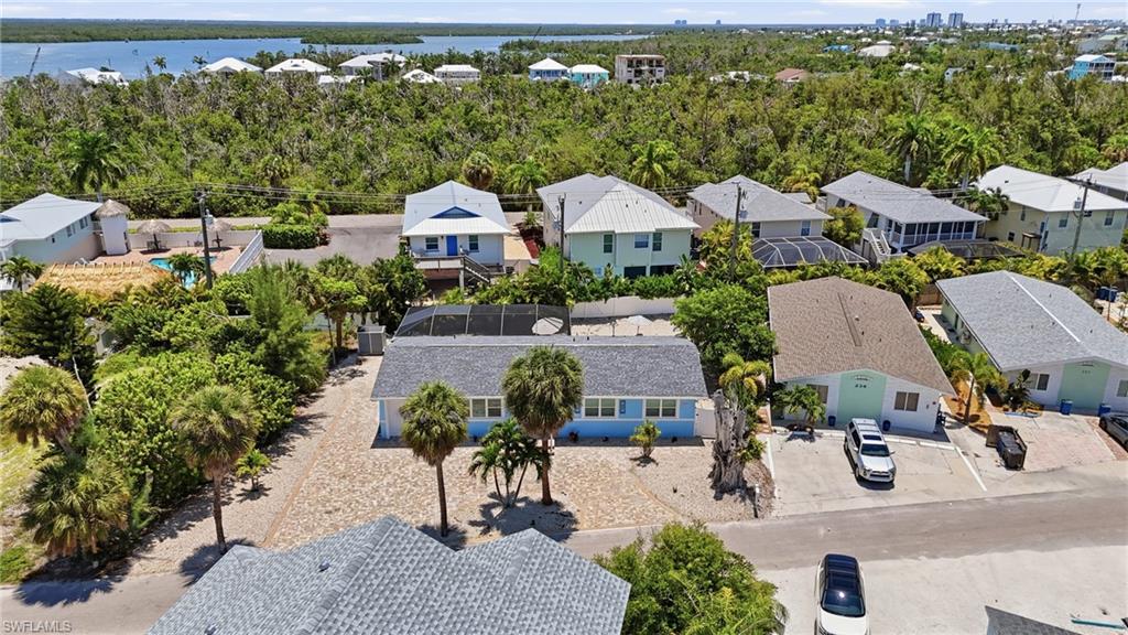 Aerial perspective showcasing a residential area with a prominent light blue single-story home featuring a gray shingle roof and a screened-in pool enclosure - Virtually Edited Image