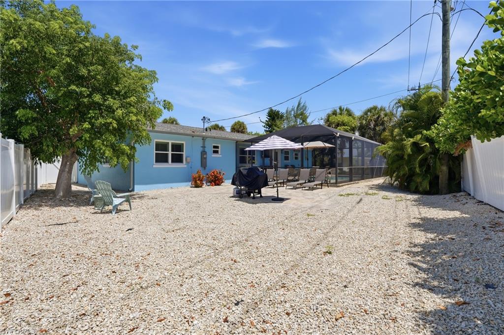 Spacious gravel yard featuring a large mature tree, white privacy fencing, and a screened-in pool enclosure - Virtually Edited Image