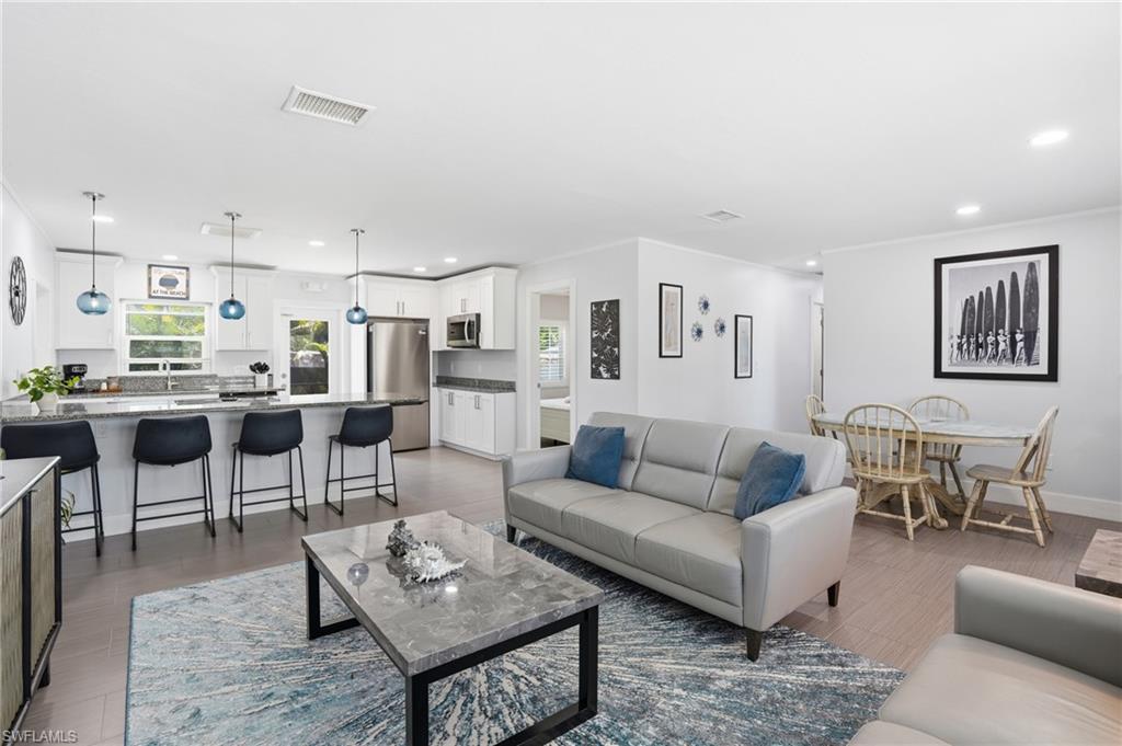 Open-concept living space featuring wood-finish flooring, recessed lighting, and a white color palette - Virtually Edited Image