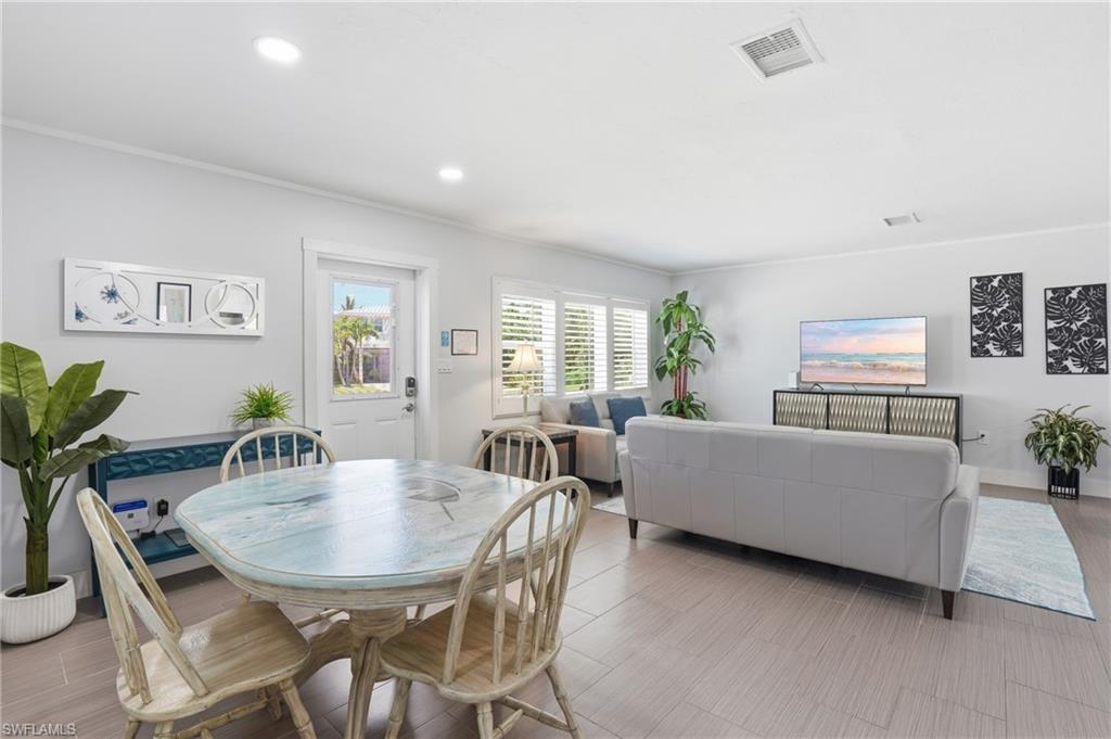 Open-concept living area featuring light-toned tile flooring, recessed lighting, and white plantation shutters - Virtually Edited Image