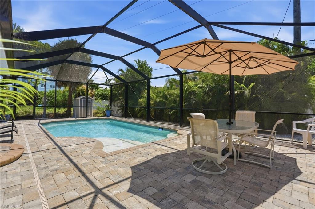 Screened-in pool area featuring a rectangular pool with integrated steps, a paver patio, and mature tropical landscaping beyond the enclosure - Virtually Edited Image