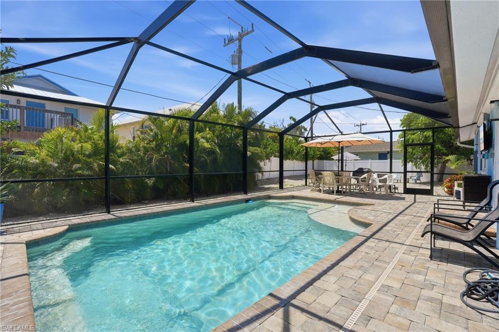 Screened swimming pool area with paver decking, integrated sun shelf, and mature perimeter landscaping - Virtually Edited Image