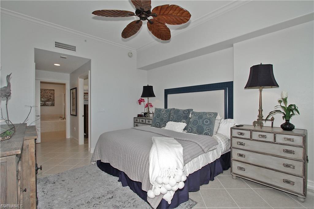 Bedroom with light tile patterned floors, ornamental molding, ensuite bathroom, and a ceiling fan