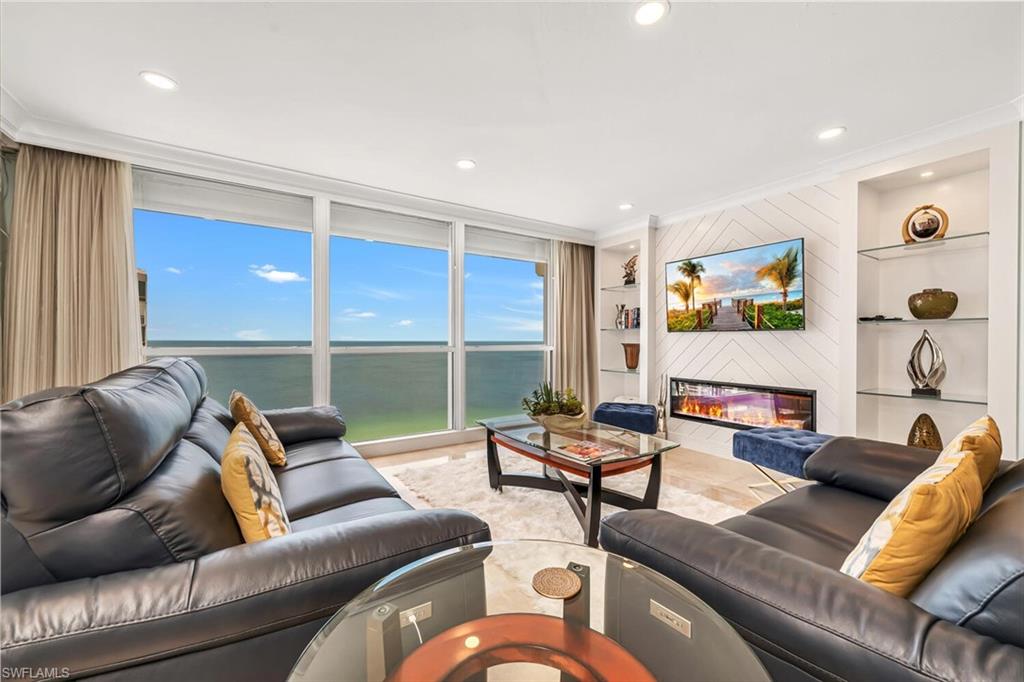 Living room featuring a glass covered fireplace, built in shelves, ornamental molding, and a healthy amount of sunlight