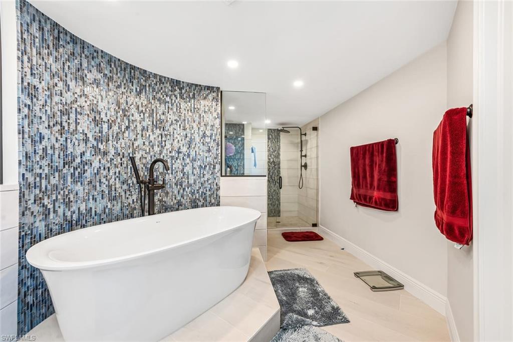 Full bathroom featuring recessed lighting, a freestanding bath, a walk in shower, tile walls, and baseboards