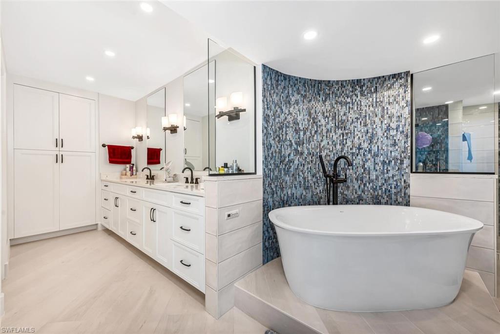 Full bathroom featuring double vanity, tile walls, a freestanding tub, and a sink