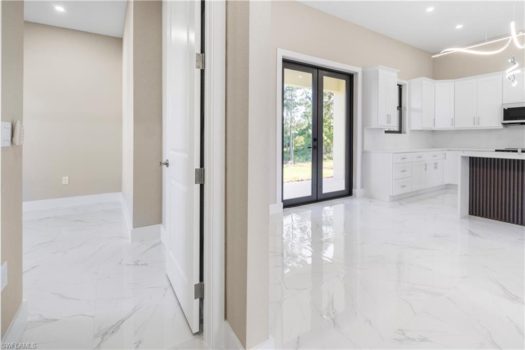 Kitchen with french doors, light marble finish floors, white cabinets, white microwave, and pendant lighting