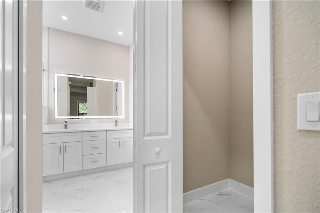 Bathroom with double vanity, light marble finish flooring, and recessed lighting