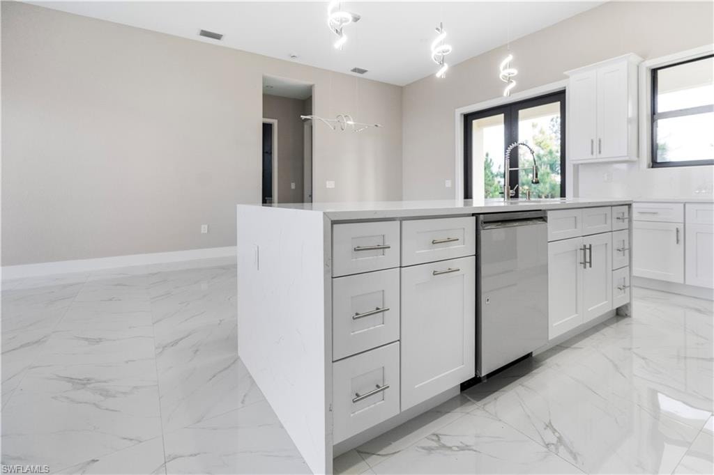 Kitchen with a kitchen island with sink, dishwasher, white cabinetry, light stone counters, and decorative light fixtures