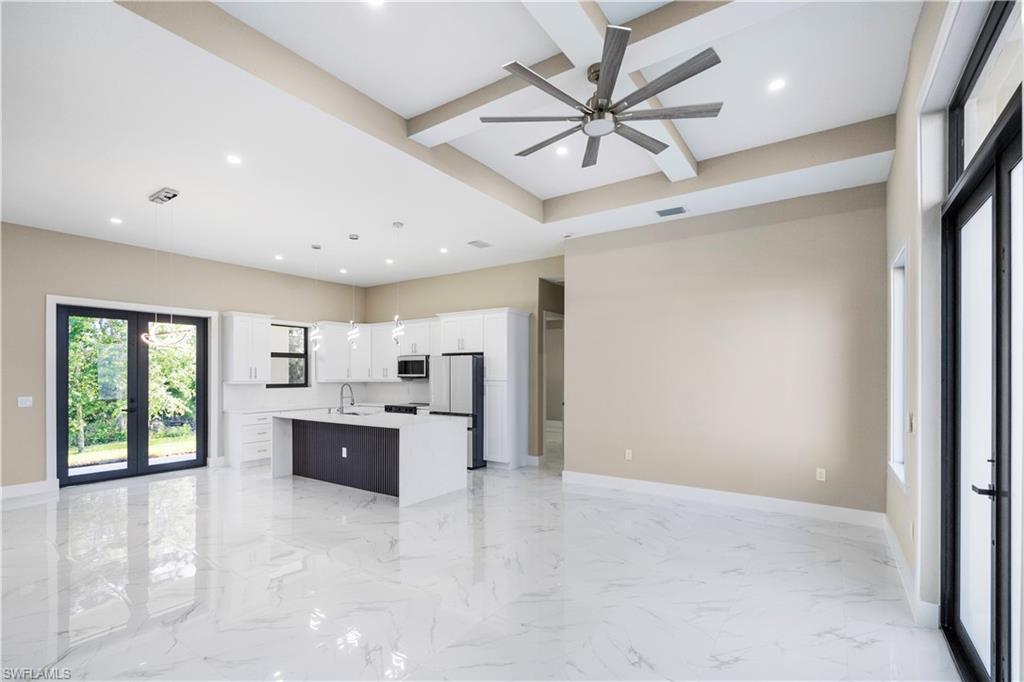 Kitchen with open floor plan, french doors, a center island with sink, light marble finish flooring, and beam ceiling
