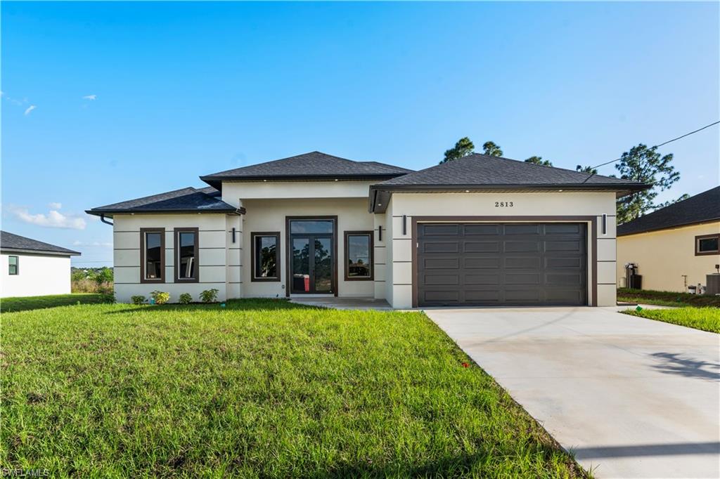 Prairie-style home featuring a garage, driveway, stucco siding, and a front lawn