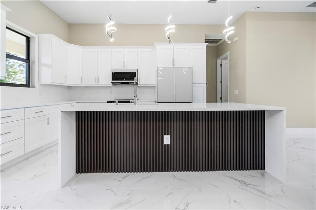 Kitchen with a kitchen island with sink, freestanding refrigerator, white cabinetry, and light stone counters
