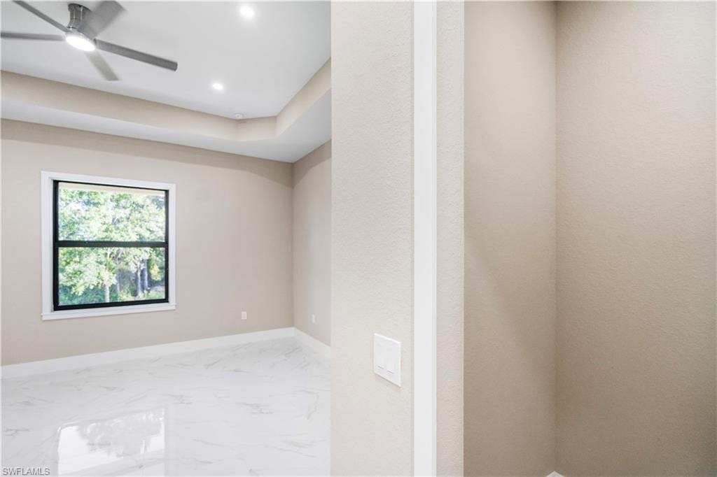 Empty room featuring light marble finish flooring, a ceiling fan, recessed lighting, and a tray ceiling
