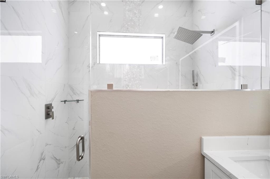 Full bath with a marble finish shower, vanity, and healthy amount of natural light