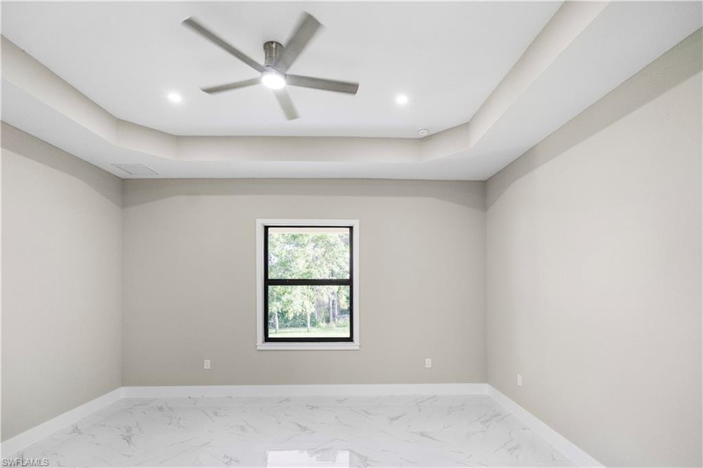 Spare room featuring a tray ceiling, light marble finish flooring, ceiling fan, and recessed lighting