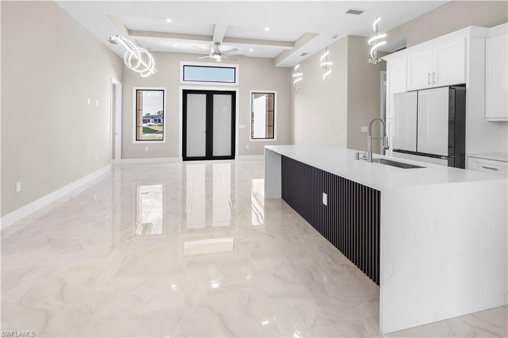 Kitchen featuring light stone counters, freestanding refrigerator, open floor plan, white cabinets, and coffered ceiling