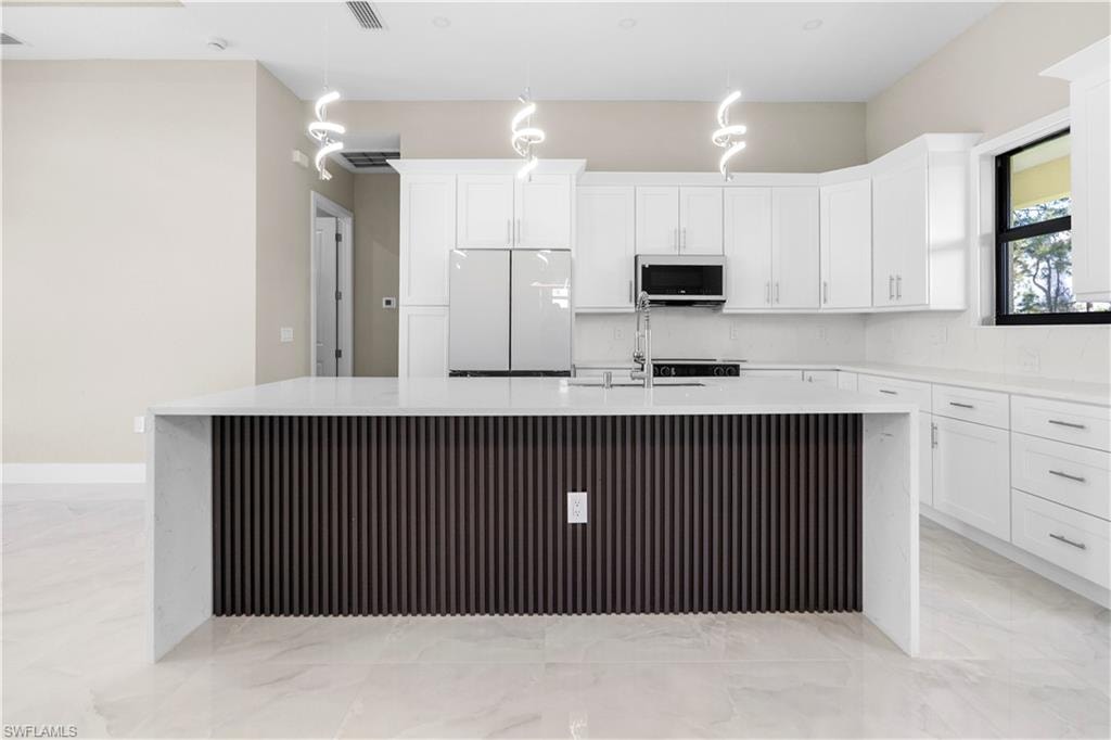Kitchen with a large island, white appliances, light stone countertops, and white cabinets