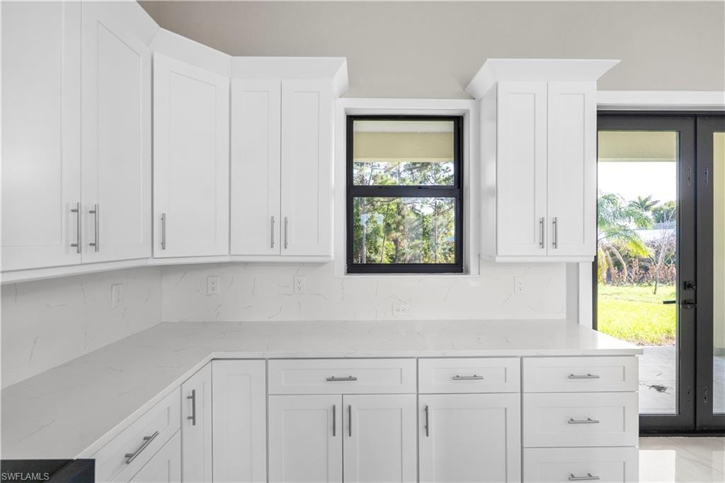 Kitchen with white cabinets, light stone countertops, decorative backsplash, and french doors