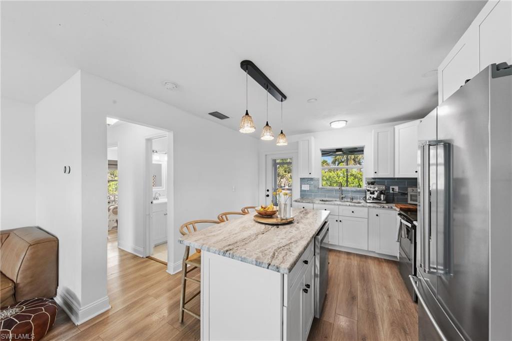 Kitchen with a breakfast bar area, white cabinets, stainless steel appliances, a center island, and light wood-style flooring