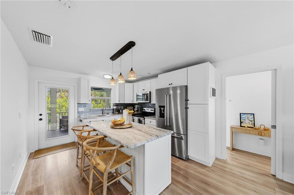 Kitchen featuring a breakfast bar, stainless steel appliances, light wood finished floors, and light stone countertops