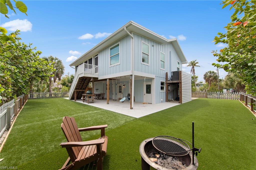 Back of house featuring board and batten siding, a patio, a fenced backyard, a fire pit, and a balcony