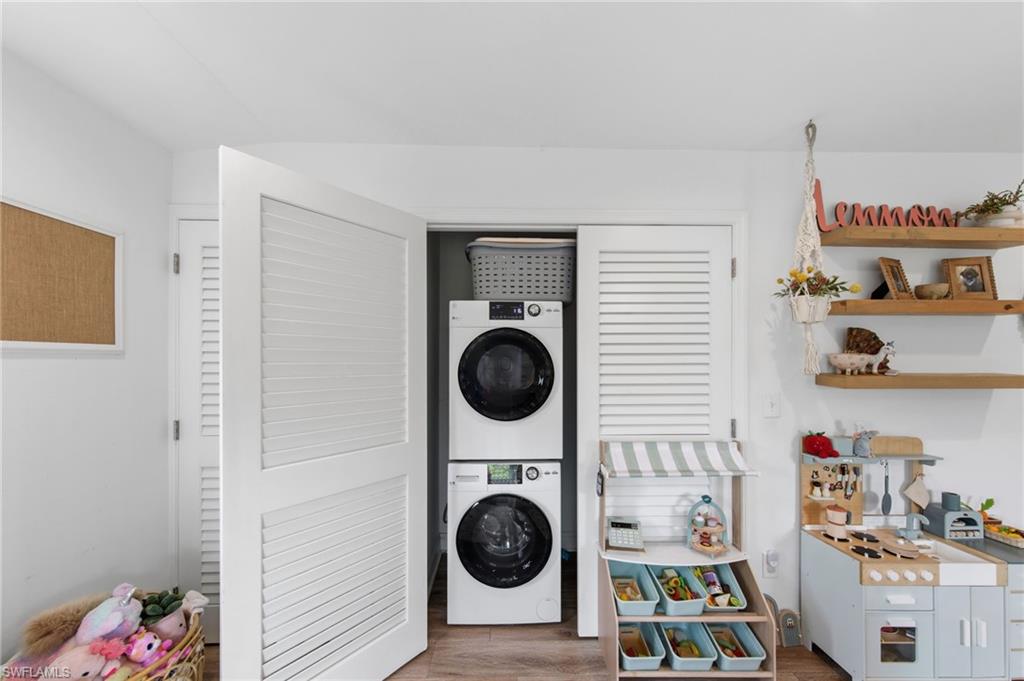 Laundry area with stacked washing machine and dryer and wood finished floors