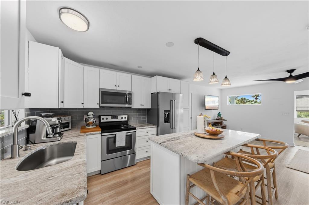Kitchen featuring stainless steel appliances, white cabinetry, a center island, backsplash, and a kitchen bar