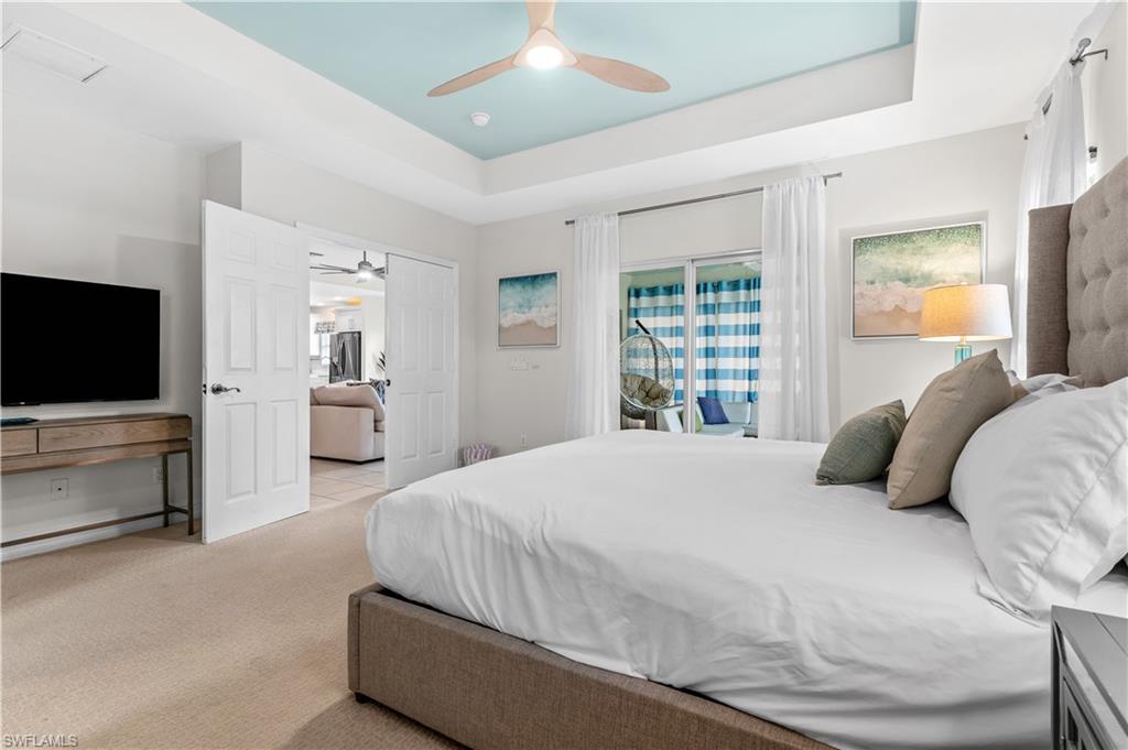 Carpeted bedroom featuring a tray ceiling with a ceiling fan, direct patio access via sliding glass doors, white paneled double doors, and a built-in entertainment console