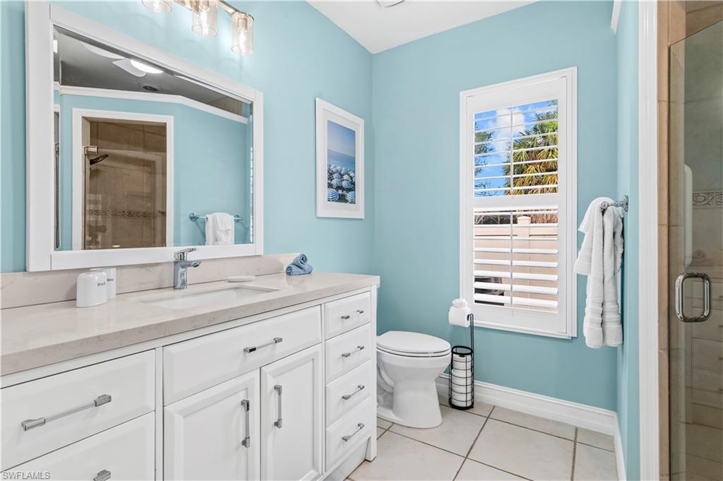 Bathroom featuring a vanity with an integrated sink and light-toned countertop, an octagonal wall mirror, a toilet, a shower with a curved rod, and beige wall tiling