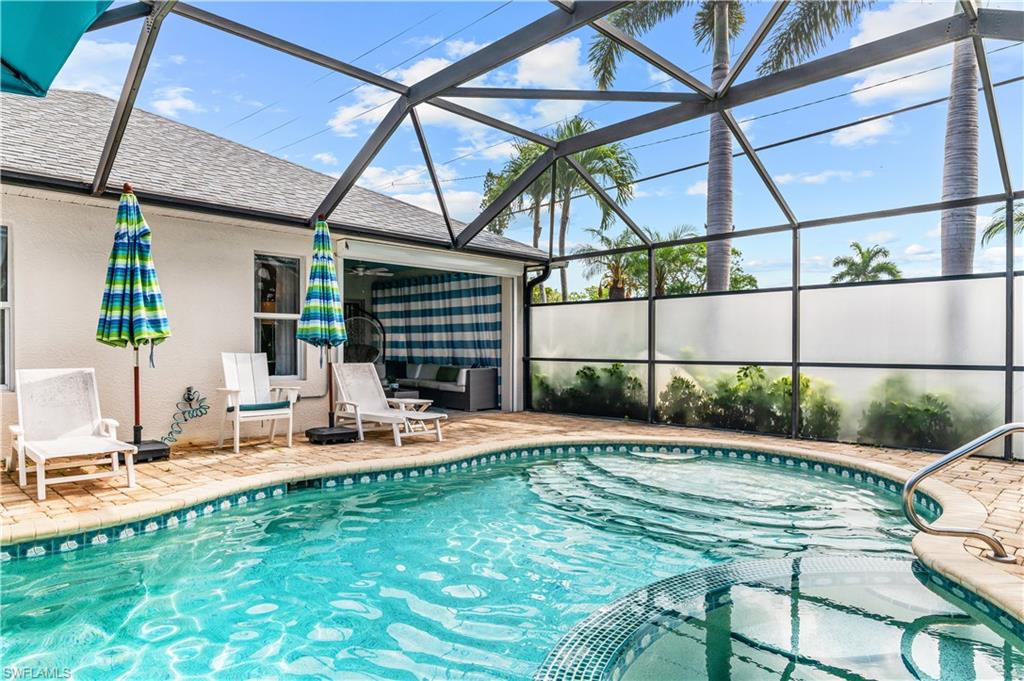 Screened pool enclosure featuring a curved pool with an integrated spa, brick paver decking, and a covered lanai