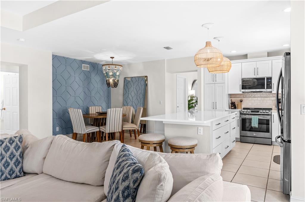 Open-concept interior featuring a modern kitchen with white cabinetry and stainless steel appliances, a center island with countertop seating, and tile flooring