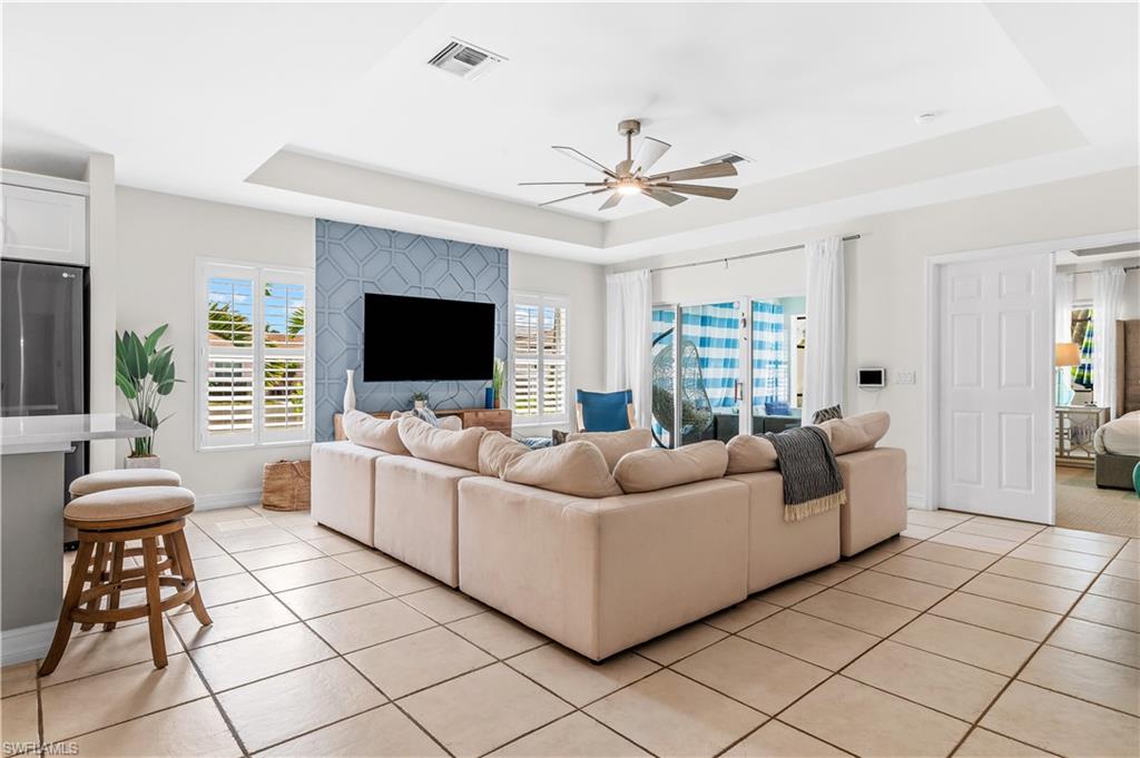 Spacious open-concept living area featuring light-toned tile flooring, a tray ceiling with a ceiling fan, and sliding glass doors to the exterior