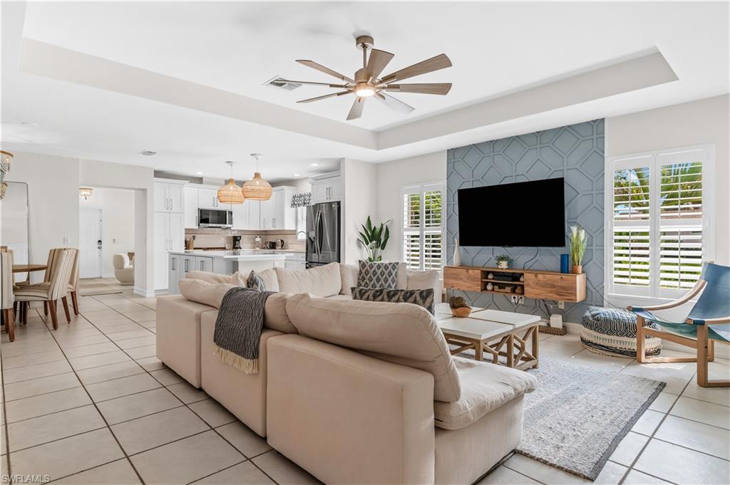 Living area featuring a detailed accent wall with geometric patterning, a tray ceiling, and a ceiling fan