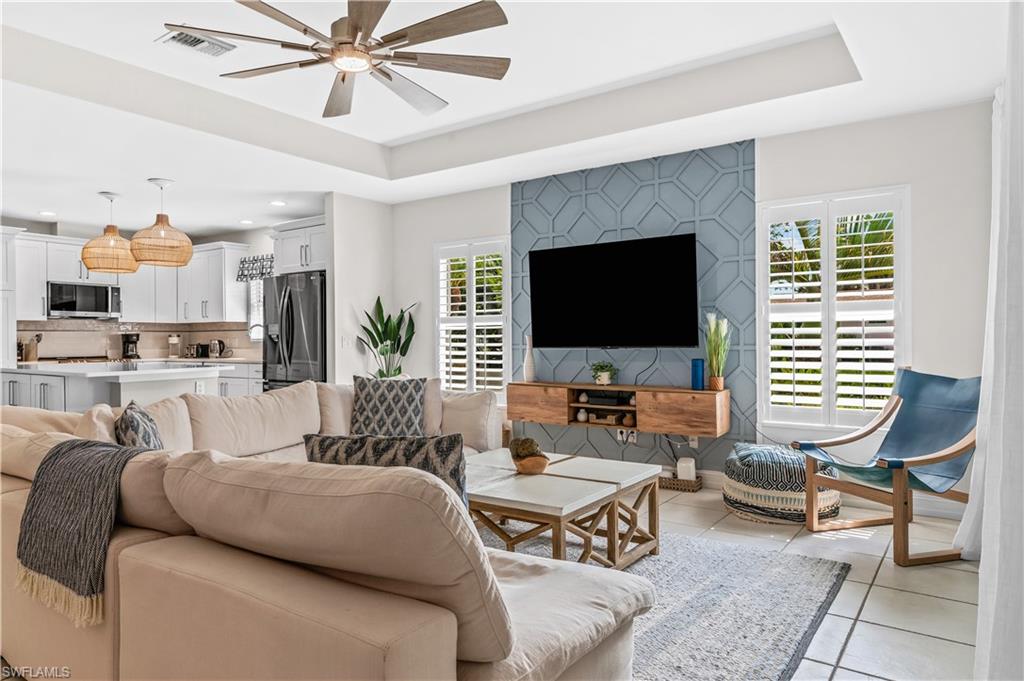 Bright interior space featuring a tray ceiling with a ceiling fan, tile flooring, and plantation shutters