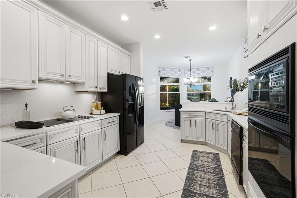 Kitchen with black appliances, a peninsula, white cabinetry, suspended lighting, and light tile patterned floors