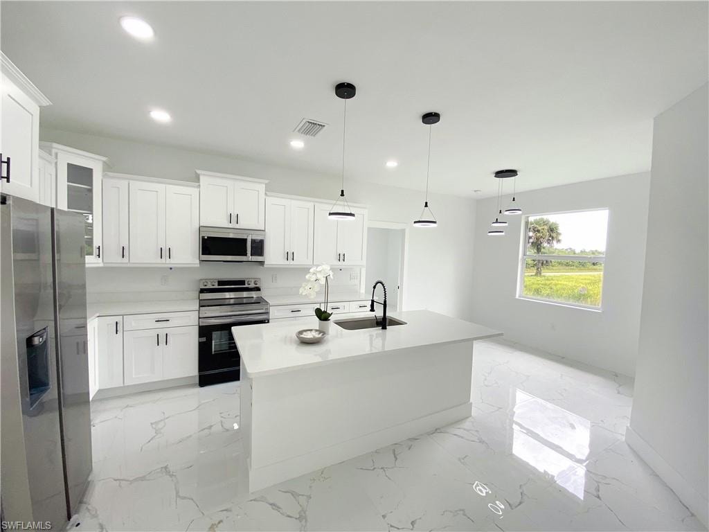 Kitchen featuring stainless steel appliances, decorative light fixtures, a center island with sink, white cabinets, and light stone countertops. Photos are of a staged model or similar plan. Features and finishes may vary.