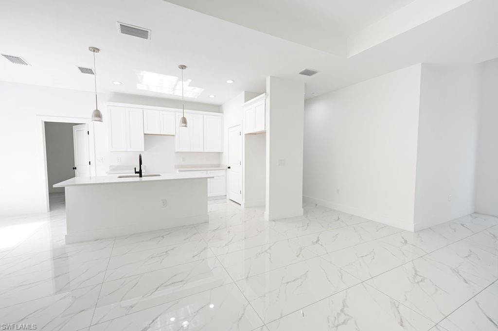 Kitchen with white cabinets, a center island with sink, hanging light fixtures, open floor plan, and light marble finish floors. Photos are of a staged model or similar plan. Features and finishes may vary.