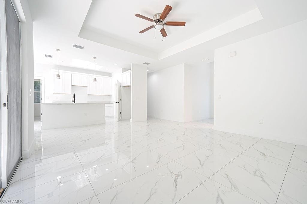 Unfurnished living room featuring a tray ceiling, ceiling fan, and light marble finish flooring. Photos are of a staged model or similar plan. Features and finishes may vary.