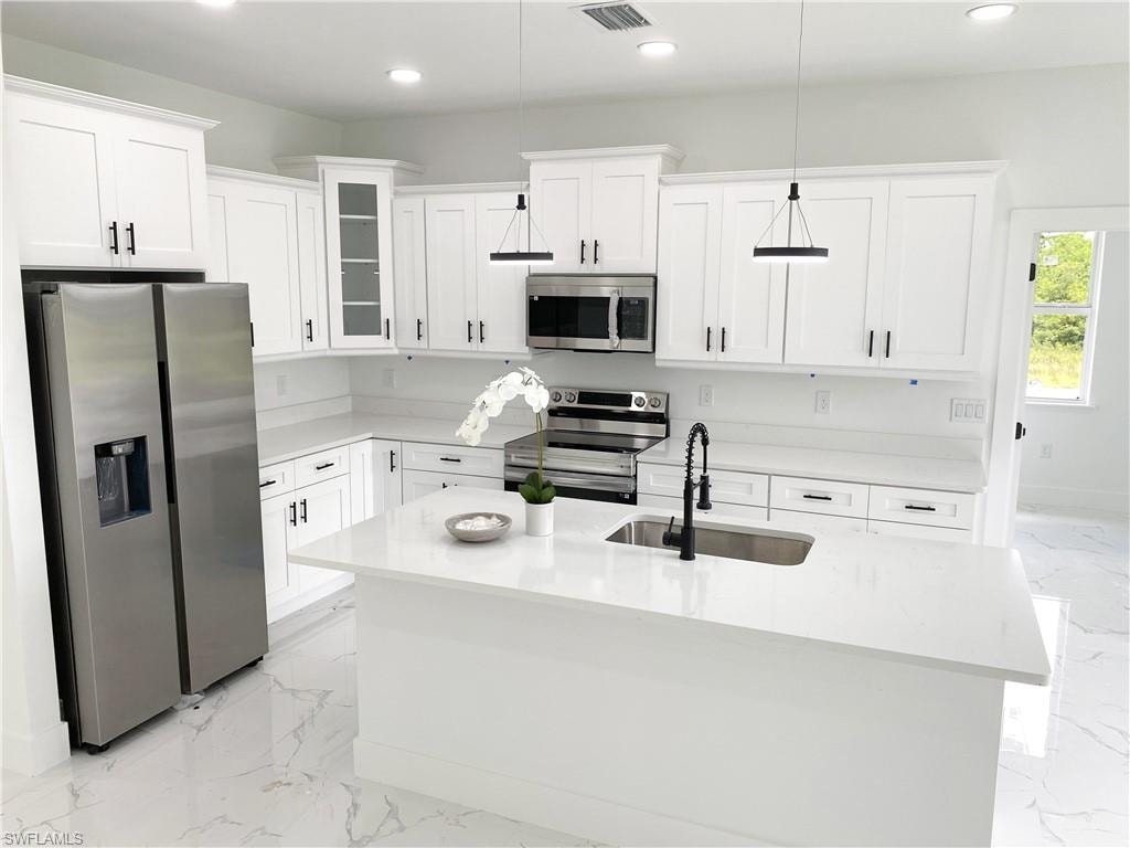 Kitchen with stainless steel appliances, light stone counters, an island with sink, glass insert cabinets, and hanging light fixtures.Photos are of a staged model or similar plan. Features and finishes may vary.