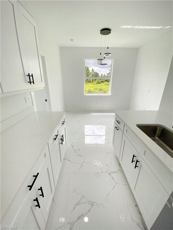 Kitchen featuring white cabinetry, light stone countertops, pendant lighting, and light marble finish floors. Photos are of a staged model or similar plan. Features and finishes may vary.